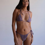 Woman wearing a purple bikini against a plain background