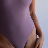 Woman wearing a mauve swimsuit against a plain background